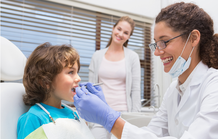 Professional pediatric dentist giving dental exam to young boy in Hamilton dental office