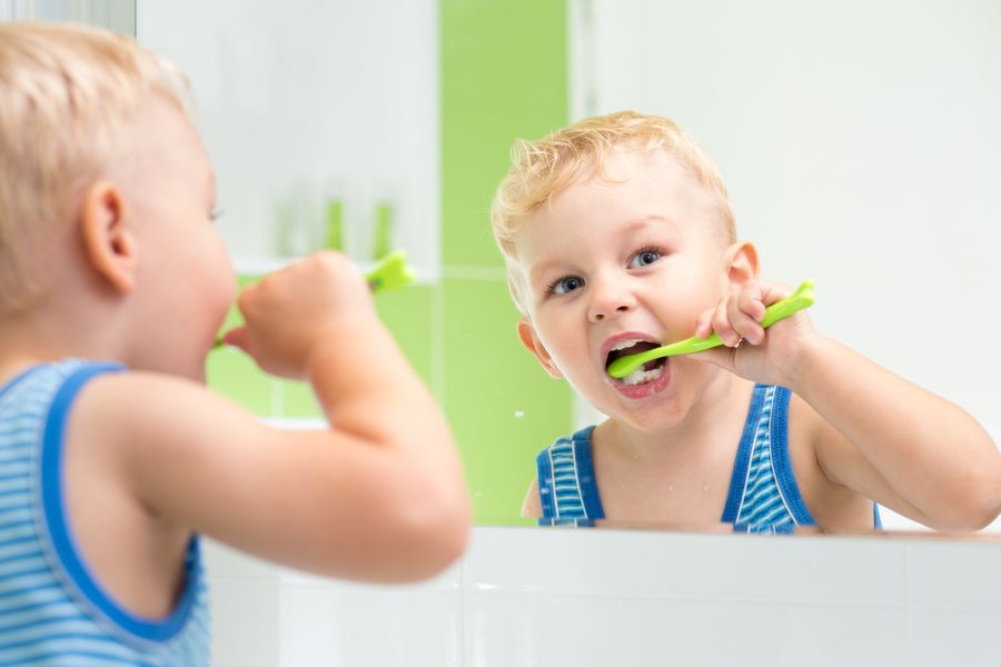 Blond child brushing teeth in mirror of Hamilton washroom