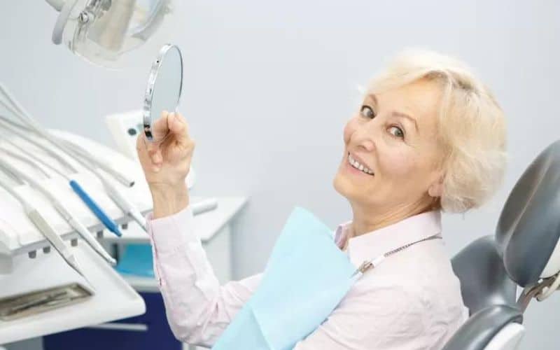 Happy elderly patient checking dental implants with mirror in Hamilton dental office