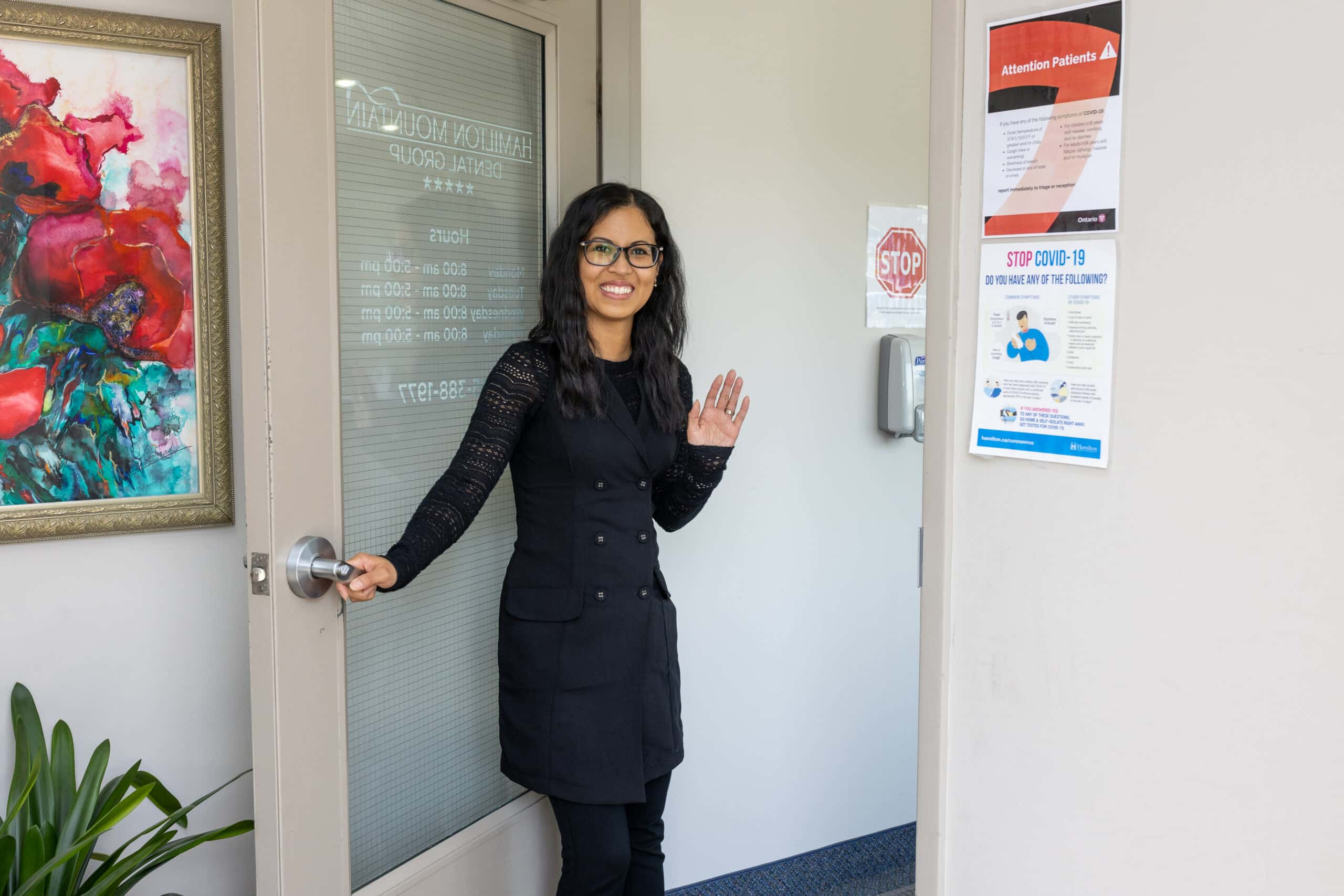 A woman in glasses standing in front of a door in Dentist Hamilton.