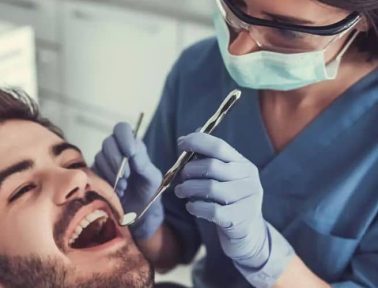 Hamilton dental hygienist using dental mirror to check bearded patient for cavities