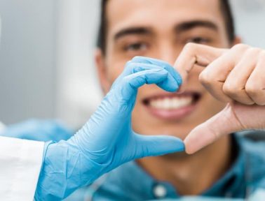 A person wearing blue medical gloves forms a heart shape with their hands alongside another smiling person, promoting oral health at Hamilton Mountain Dental.